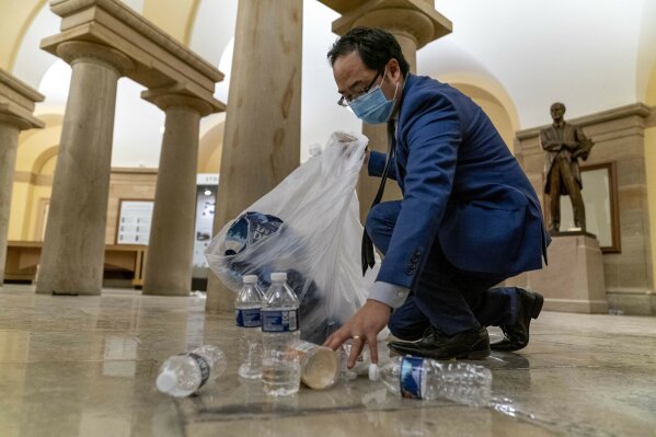 Rep. Andy Kim, D-N.J., cleans up debris and trash strewn across the floor in the early morning hours of Thursday, Jan. 7, 2021, after protesters stormed the Capitol in Washington, on Wednesday. (AP Photo/Andrew Harnik)