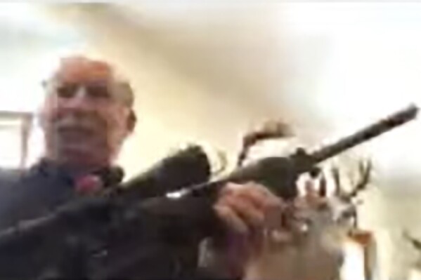 In this image from a Zoom meeting provided by the Grand Traverse, Mich., County Board of Commissioners, Grand Traverse County Commissioner Ron Clous holds a rifle at his home during a county commissioners meeting, Jan. 20, 2021, in Michigan. (Grand Traverse County Board of Commissioners via AP, File)