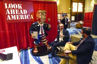 FILE - In this Feb. 26, 2021, file photo, Look Ahead America sponsor Matt Braynard, center, talks to conference attendees at his booth in the merchandise show with a statue of former president Donald Trump at the Conservative Political Action Conference (CPAC) in Orlando, Fla. (AP Photo/John Raoux, File)