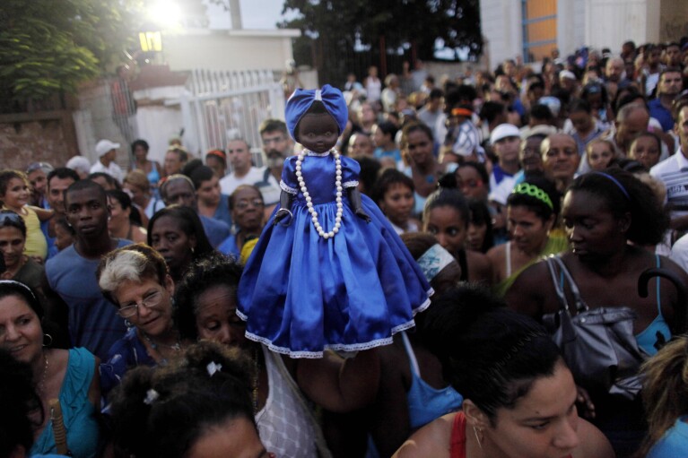 FILE - A woman holds up a doll representing the Virgin of Regla during a procession in her honor in Regla, Cuba, Sept. 7, 2010. The black virgin is honored on the same day as Cuba's patron saint the Virgin of Charity, both of which are also recognized as powerful deities in the African-influenced religion of Santeria. (AP Photo/Javier Galeano, File)