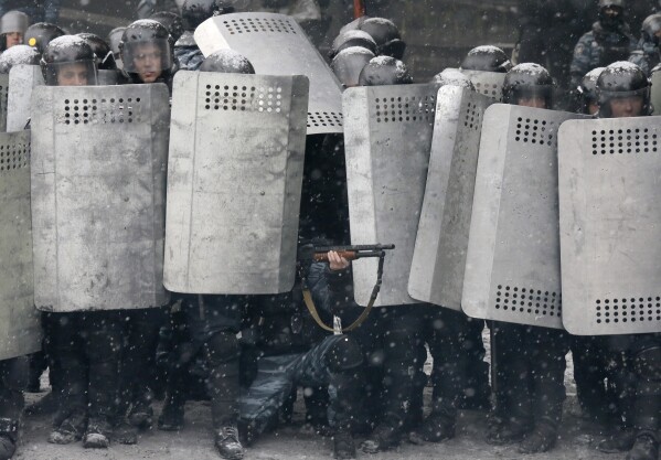 FILE - In this file photo taken on Jan. 22, 2014, a police officer aims his shotgun during clashes with protesters in central Kyiv, Ukraine. On Nov. 21, 2023, Ukraine marks the 10th anniversary of the uprising that eventually led to the ouster of the country’s Moscow-friendly president. (AP Photo/Efrem Lukatsky, file)