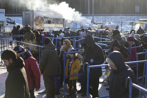 FILE - Migrants queue to receive hot food at a logistics center at the checkpoint logistics center "Bruzgi" at the Belarus-Poland border near Grodno, Belarus, on Dec. 22, 2021. Poland’s conservative governing party was hoping to make migration a key campaign theme ahead of the country’s national election. But not like this. The Law and Justice party is being rocked by reports that Polish consulates issued visas in Africa and Asia in exchange for bribes, opening the door for migrants to enter the European Union. (AP Photo/Pavel Golovkin)