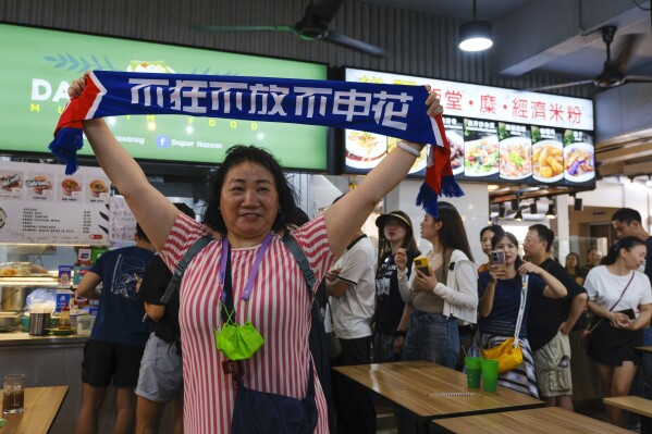 2024 年 6 月 14 日星期五，一名中国球迷在新加坡门将哈桑·桑尼的小吃摊前拍照。桑尼在本周的一场比赛中表现出色，间接帮助中国队晋级 2026 年世界杯预选赛第三轮，中国球迷纷纷向桑尼的小吃摊表达喜爱。（美联社/Tim Chong 摄）