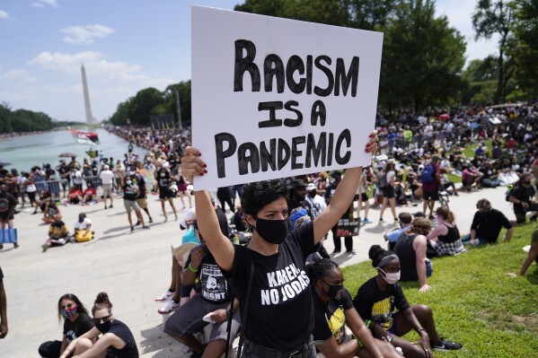 FILE - Priscilla Duerrero holds a sign reading "Racism Is A Pandemic" during the March on Washington, Friday, Aug. 28, 2020, at the Lincoln Memorial in Washington, on the 57th anniversary of the Rev. Martin Luther King Jr.'s "I Have A Dream" speech. (AP Photo/Julio Cortez, File)