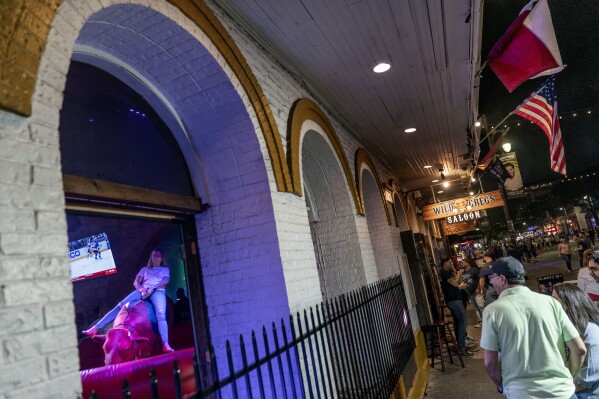 A patron rides a mechanical bull at a bar lining a popular nightlife district in Austin, Texas, Saturday, April 22, 2023. Since the early 1600s, ranchers raising cattle would cement the image of longhorn steers, rugged cowboys and awe-inspiring vistas into the nation's consciousness as what it means to be a Texan. The state has changed dramatically since then, but that image remains today and keeps beef in the forefront of life in Texas. (AP Photo/David Goldman)