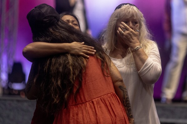 Attendees embrace during a church service at King's Cathedral in Kahului on the island of Maui, Hawaii Sunday, Aug. 13, 2023. The church has been converted into an emergency shelter and destruction center since the devastating wildfires that affected multiple regions on the island. (Stephen Lam/San Francisco Chronicle via AP)