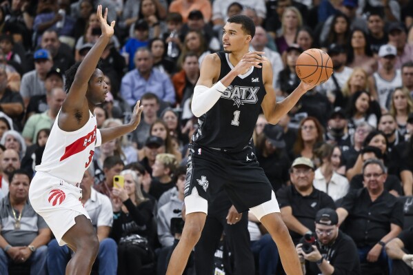 San Antonio Spurs' Victor Wembanyama (1) looks to pass the ball as he is defended by Toronto Raptors' O.G. Anunoby, left, during the second half of an NBA basketball game, Sunday, Nov. 5, 2023, in San Antonio. (AP Photo/Darren Abate)