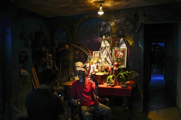 Juan Gonzalez sits next to his altar adorned with religious statues of Afro-Cuban Santeria deities, including "Ochun" and a photo of the late Cuban leader Fidel Castro, at his home in El Cobre, Cuba, Saturday, Feb. 10, 2024. Ochun, considered the goddess of female sensuality and motherhood, is associated with the Catholic Virgin of Charity of Cobre, Cuba's patron saint. (AP Photo/Ramon Espinosa)