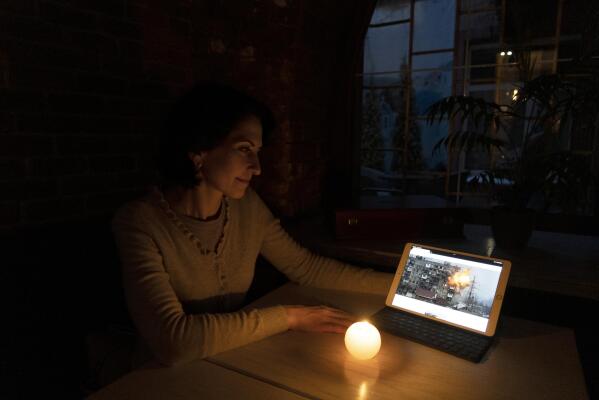 Inna Nepomnyshaya looks at a photo of her apartment building at 110 Mytropolytska St. in Mariupol, Ukraine, as it was struck by Russian tank fire in March 11, 2022, during an interview in Dnipro, Ukraine, on Nov. 22, 2022, where she has settled after fleeing her home. The shell shattered the walls of Nepomnyshaya’s apartment and obliterated those of the neighbors above, below and behind her. (AP Photo/Vasilisa Stepanenko)