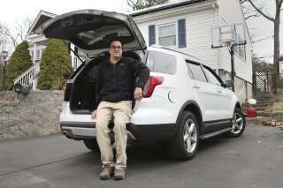 Tim Miranda, a software company manager currently working from home during the coronavirus outbreak, sits in his vehicle outside his Chelmsford, Mass. home, Thursday, April 2, 2020. Miranda, who usually works about 30 miles away in Cambridge, Mass., is donating his weekly $100 out of pocket commuting expenses to local charities that help provide meals and assistance to youth. (AP Photo/Charles Krupa)