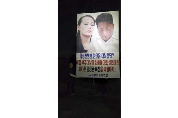 In this photo provided by Fighters for a Free North Korea, Park Sang-hak holds a placard carrying pictures of North Korean leader Kim Jong Un and his sister Kim Yo Jong in Ganghwa, South Korea Sunday, Sept. 4, 2022. Park said he has again flown huge balloons carrying COVID-19 relief items and an anti-North Korea placard across the tense inter-Korean border, despite the North’s recent warning of a deadly attack over his activities. A part of letters read "Let's eradicate Kim Jong Un and (his sister) Kim Yo Jong." (Fighters for a Free North Korea via AP)