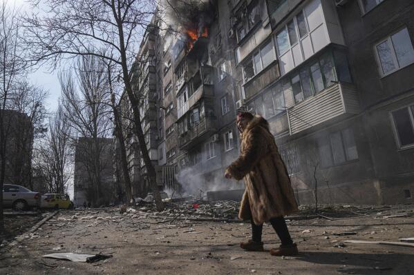 FILE - A woman walks past a burning apartment building after shelling in Mariupol, Ukraine, Sunday, March 13, 2022. As milestones go, the first anniversary of Russia's invasion of Ukraine is both grim and vexing. It marks a full year of killing, destruction, loss and pain felt even beyond the borders of Russia and Ukraine. (AP Photo/Evgeniy Maloletka, File)