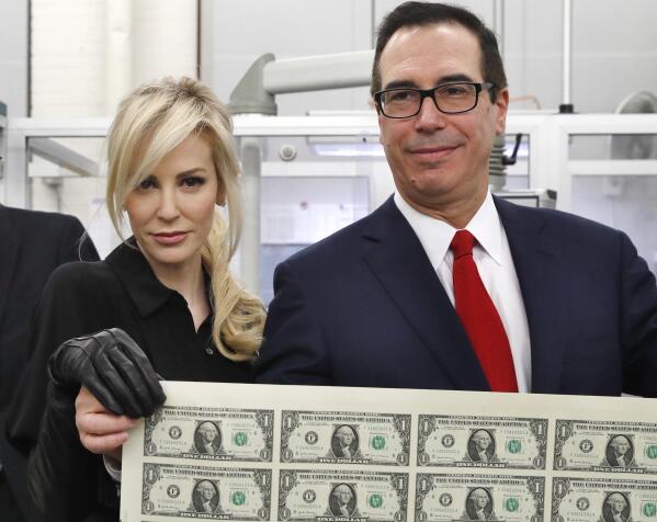 Treasury Secretary Steven Mnuchin, right, and his wife Louise Linton, hold up a sheet of new $1 bills, the first currency notes bearing his and U.S. Treasurer Jovita Carranza's signatures, Wednesday, Nov. 15, 2017, at the Bureau of Engraving and Printing (BEP) in Washington. The Mnuchin-Carranza notes, which are a new series of 2017, 50-subject $1 notes, will be sent to the Federal Reserve to issue into circulation. At left is BEP Director Leonard Olijar. (AP Photo/Jacquelyn Martin)
