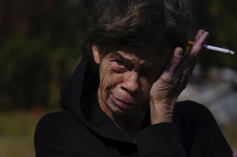 Lisa McGuire wipes away a tear on Thursday, Dec. 7, 2023, as she describes a fire that engulfed her home, killing her two dogs in Prichard, Ala. When a neighbor called her about the fire, she said she rushed home to find Prichard firefighters standing with an empty hose attached to a hydrant. (AP Photo/Brynn Anderson)