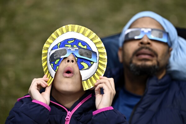 Dezaray Butts and her father Douglas wear solar eclipse glasses as they observe the partial phase of a total solar eclipse, in Kingston, Ontario, Monday, April 8, 2024. (Justin Tang/The Canadian Press via AP)