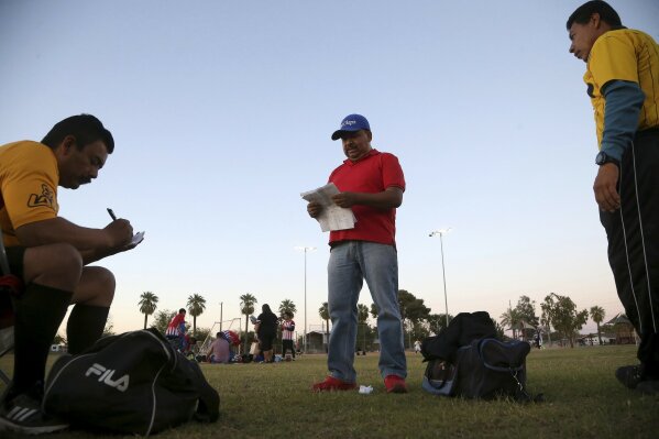FILE - In this April 17, 2019, file photo Antonio Velasquez, center, a pastor and director of the Maya Chapin soccer league, gives referees their game assignments in Phoenix. Velasquez says before the Trump administration announced a crackdown on immigrants using government social services, people lined up before sunrise outside a state office in his neighborhood to sign up for food stamps and Medicaid.   (AP Photo/Ross D. Franklin, File)