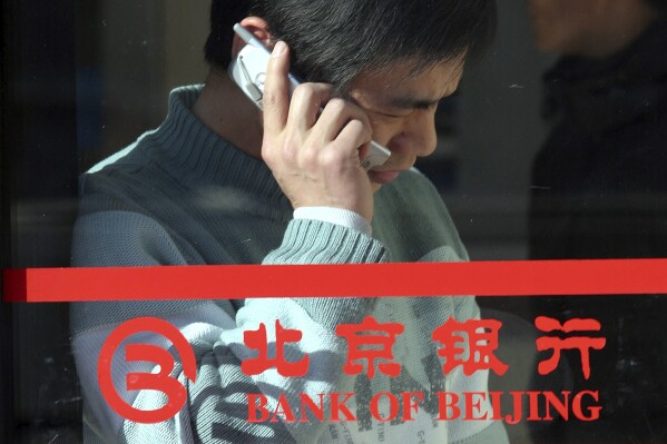 FILE - A Chinese man uses his mobile phone near the logo for the Bank of Beijing in Beijing Jan. 29, 2005. The former chairman of state-owned Bank of Beijing is under investigation for corruption, according to an official notice Friday, March 1, 2024, the latest in a series of graft investigations focused on the country's financial sector. (AP Photo, File)