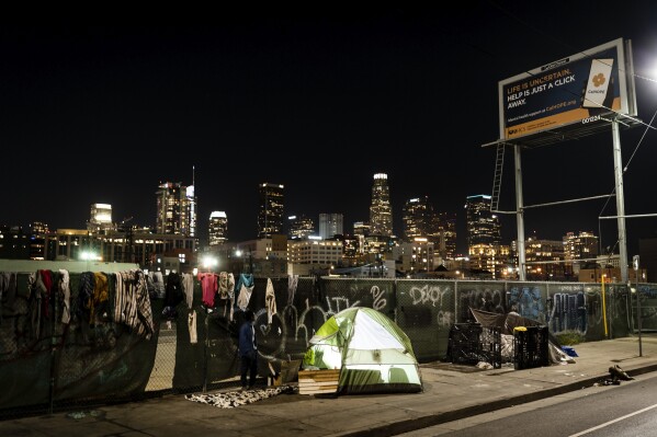 In this photo illuminated by an off-camera flash, a homeless person's tent is backdropped by the skyline of Los Angeles, Wednesday, Feb. 8, 2023. A new study by the University of California, San Francisco shows that homeless people in California were struggling with poor health and deep poverty before becoming homeless. The study released Tuesday, June 20, by the Benioff Homelessness and Housing Initiative aims to provide a comprehensive picture of adult homelessness in a state that has 30% of the country's homeless. (AP Photo/Jae C. Hong)