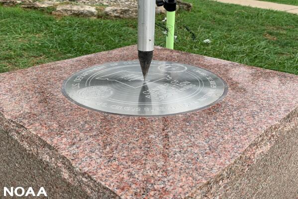 This photo provided by NOAA shows the tip of a tripod resting on the center of the 2020 Center of Population Commemorative Survey mark, as part of a GPS survey to determine the precise latitude, longitude, and height of the mark on Sept. 14, 2022 in Hartville, Mo.  The U.S. Census Bureau announced the nation’s new center of population in 2020 to be in Hartville, in the Ozark Mountains.  (NOAA via AP)