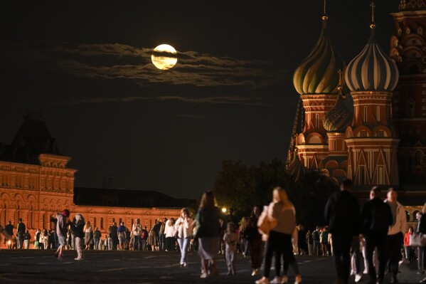 The August Super Blue Moon sets behind a historical building and the St. Basil's Cathedral, right, as people walk in Red Square in Moscow, Russia, Wednesday, Aug. 30, 2023. (AP Photo/Alexander Zemlianichenko)