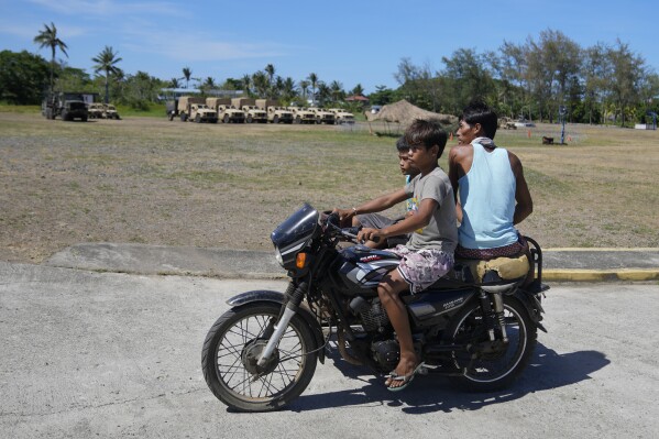 FILE - Filipinos drive their tricycle past U.S. military vehicles at the Naval Base Camilo Osias in Santa Ana, Cagayan province, northern Philippines on May 6, 2024. The United States and the Philippines, which are longtime treaty allies, have identified the far-flung coastal town of Santa Ana in the northeastern tip of the Philippine mainland as one of nine mostly rural areas where rotating batches of American forces could encamp indefinitely and store their weapons and equipment within local military bases under the Enhanced Defense Cooperation Agreement, or EDCA. (AP Photo/Aaron Favila, File)
