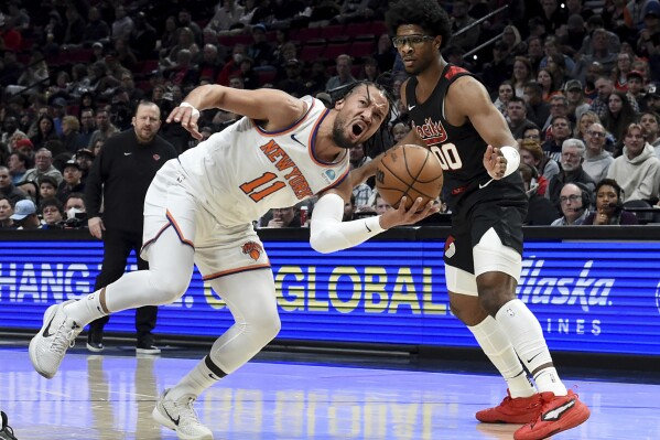New York Knicks guard Jalen Brunson, left, drives to the basket against Portland Trail Blazers guard Scoot Henderson, right, during the first half of an NBA basketball game in Portland, Ore., Thursday, March 14, 2024. (AP Photo/Steve Dykes)