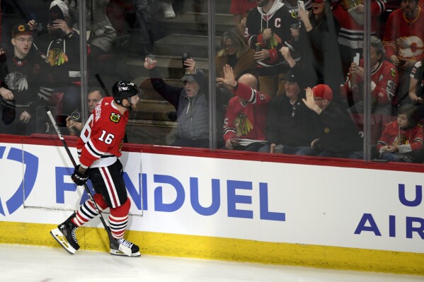 Chicago Blackhawks' Jason Dickinson (16) celebrates with fans after scoring a goal during the first period of an NHL hockey game against the Calgary Flames Tuesday, March 26, 2024, in Chicago. (AP Photo/Paul Beaty)