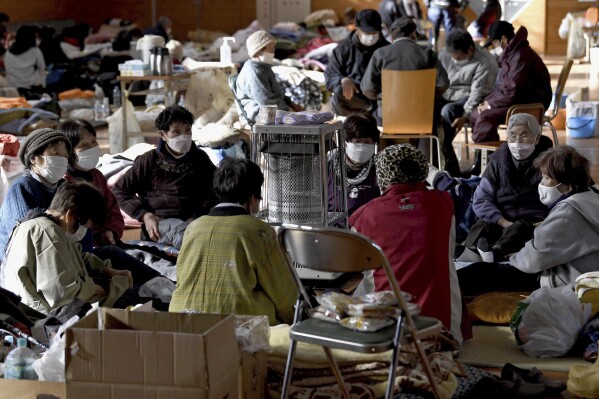 Evacuees warm up together in a shelter in the earthquake-hit Anamizu, Ishikawa prefecture, Monday, Jan. 8, 2024. Thousands of people made homeless overnight are living in weariness and uncertainty on the western coast of Japan a week after powerful earthquakes hit the region. (Kyodo News via AP)