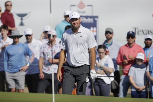 Scottie Scheffler looks at the pin before hitting out of the bunker on the 18th green during the first round of the Houston Open golf tournament Thursday, March, 28, 2024, in Houston. (AP Photo/Michael Wyke)