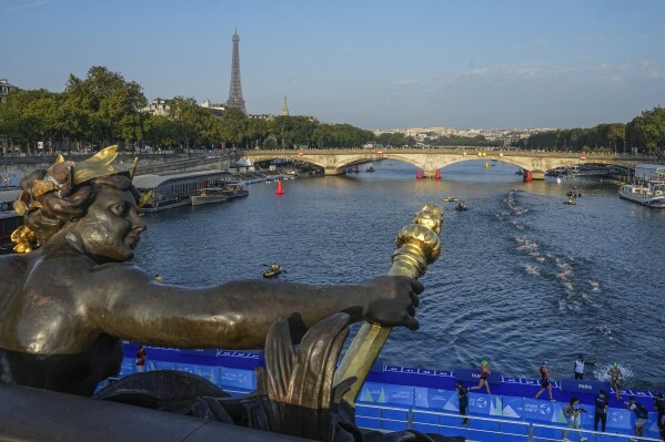 Athletes dive and swim in the Seine river from the Alexander III bridge on the first leg of the women's triathlon test event for the Paris 2024 Olympics Games in Paris, Thursday, Aug. 17, 2023. In 2024. The bridge will be the setting for the finish line of the individual cycling time trials, swimming marathon, triathlon and para triathlon. (AP Photo/Michel Euler)