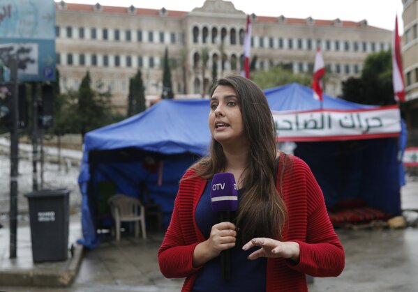 In this Thursday, Dec. 5, 2019 photo, Rima Hamdan, a Lebanese reporter for OTV a station that is backed by Lebanese President Michel Aoun, reports from a square where anti-government protesters hold ongoing protests, in downtown Beirut, Lebanon. “The protest movement has turned our lives upside down,” said Hamdan, who during one of her reports slapped a man on his hand after he pointed his middle finger to her. She said the station’s logo “is our identity even though sometimes we had to remove it for our own safety." (AP Photo/Hussein Malla)