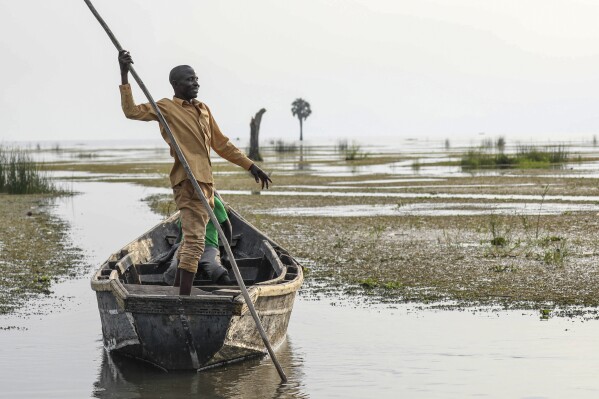 John Gafabusa, custodian of the Mutyona natural sacred site near Buliisa, Uganda, points at a water covered sacred site on Lake Albert at the Karakaba landing site, Aug. 3, 2023. As TotalEnergies invests billions into oilfield development and acquires more and more land, Bagungu people who practice traditional beliefs worry the spiritual power of at least 32 sacred natural sites in Buliisa keeps deteriorating. (AP Photo/Hajarah Nalwadda)