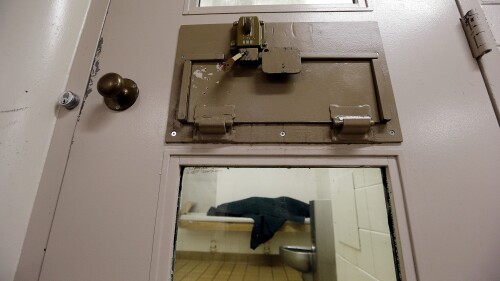 FILE - An inmate huddles under a heavy blanket on a bunk in the psychiatric unit of the Pierce County Jail in Tacoma, Wash, on Oct. 15, 2014. A federal judge has found Washington state in contempt and ordered it to pay more than $100 million in fines for failing to provide timely psychiatric services to mentally ill people who are forced to wait in jails for weeks or months. (AP Photo/Elaine Thompson, File)