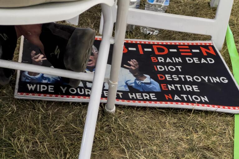 A man sits with his feet on a doormat critical of President Joe Biden during the ReAwaken America Tour at Cornerstone Church in Batavia, N.Y., Saturday, Aug. 13, 2022. (AP Photo/Carolyn Kaster)