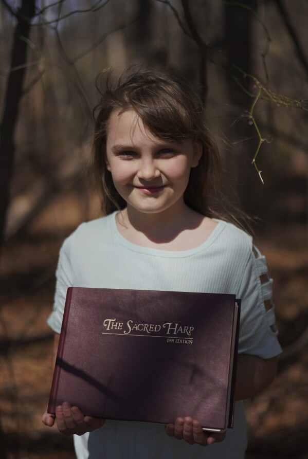 Riley McKibbin, 11, poses for a portrait with her copy of "The Sacred Harp" at Holly Springs Primitive Baptist Church in Bremen, Ga., on Saturday, March 22, 2025. (AP Photo/Jessie Wardarski)