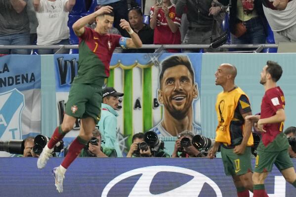 Poster with picture of Argentina's Lionel Messi hangs from a tribune as Portugal's Cristiano Ronaldo celebrates after scoring his sides first goal during the World Cup group H soccer match between Portugal and Ghana, at the Stadium 974 in Doha, Qatar, Thursday, Nov. 24, 2022. (AP Photo/Darko Bandic)