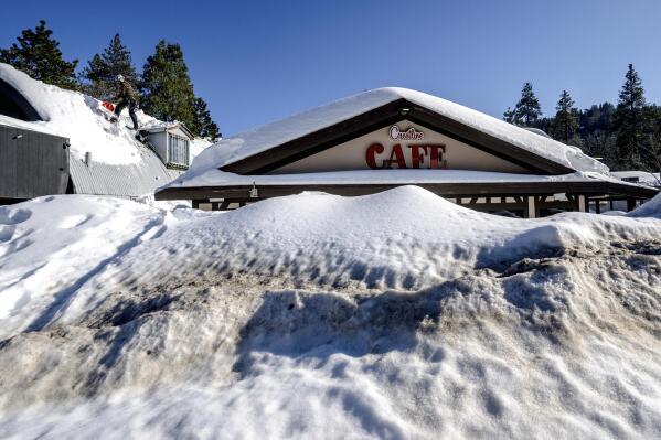A man shovels snow off the roof of a store in Crestline, Calif., Friday, March 3, 2023, as buildings remain buried in several feet of snow from recent winter storms. (Watchara Phomicinda/The Orange County Register via AP)