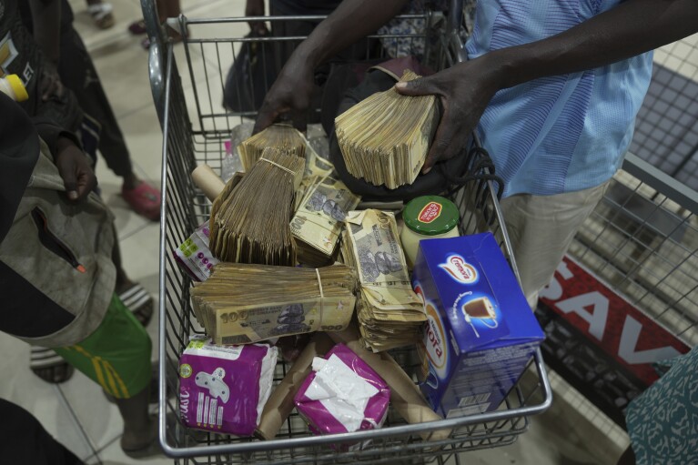 A man uses old Zimbabwean dollar notes to buy groceries in a supermarket in Harare, Thursday, April 25, 2024. Zimbabwe started circulating banknotes and coins for another new currency Tuesday in its latest attempt to solve a long-running monetary crisis that has seen the government try gold coins and a digital currency among other ideas. (AP Photo/Tsvangirayi Mukwazhi)