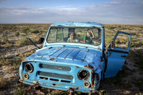 Children play inside a rusted dilapidated car along the dried-up Aral Sea, in the village of Tastubek near Aralsk, Kazakhstan, Monday, July 2, 2023. (AP Photo/Ebrahim Noroozi)