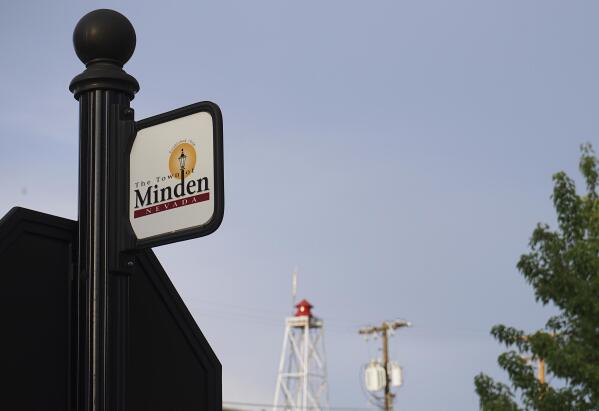 This June 30, 2021 photo shows a sign for the town of Minden, Nev. Efforts to silence the century-old siren, seen in the background, that blares every night at 6 p.m. are sparking debates over how to confront the region's history of racism and violence. The Washoe Tribe of Nevada and California associates the siren with a historic "sundown ordinance" that once made it illegal for them to be in Minden and neighboring Gardnerville after nightfall. Residents of the mostly white town defend it as a tradition that marks time and honors first responders. After state lawmakers banned the siren, the Washoe Tribe's chairman and Minden town manager agreed to move the siren to 5 p.m. but the compromise left many tribal members unsatisfied and awaits discussion at the tribal council. (AP Photo/Sam Metz)