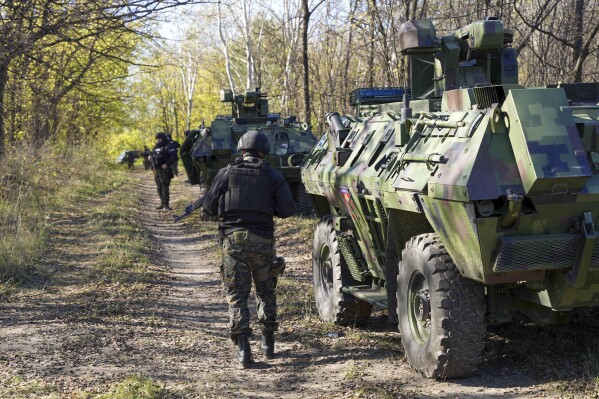 In this photo provided by the Serbian Interior Ministry, Serbian gendarmerie officers looking for migrants in a forest near the border between Serbia and Hungary, Serbia, Thursday, Nov. 2, 2023. Serbian police said Friday, Nov. 3, 2023 they made seven arrests on suspicion of smuggling people into Hungary as part of a days-long crackdown on irregular migration in the wake of a shooting last week in the border area that killed three migrants and wounded one. Reports of violence and gun battles have become common near the border between Serbia and Hungary, a European Union member state. (Serbian Ministry of Interior via AP)