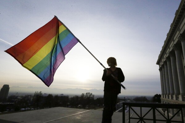 FILE - Corbin Aoyagi, a supporter of gay marriage, waves a rainbow flag during a rally at the Utah State Capitol on Jan. 28, 2014, in Salt Lake City. Utah teachers will be free to display LGBTQ+ pride flags and other social, political or religious imagery after the state House blocked a bill Monday, Feb. 26, 2024, that would have banned teachers from using their position to promote or disparage certain beliefs. (APPhoto/Rick Bowmer, File)