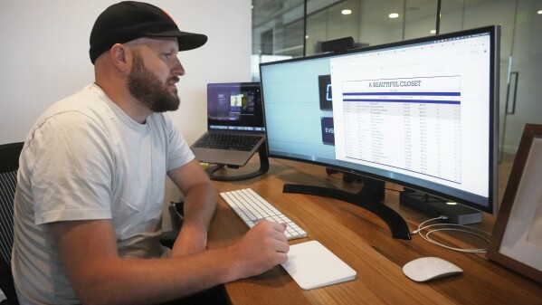 Jake Welch looks at a spreadsheet on his computer Wednesday, Aug. 2, 2023, in Salt Lake City. The 36-year-old brand director for an advertising firm calculates the cost-per-wear of his wardrobe by highlighting 200 items in a spreadsheet — excluding underwear and socks — and meticulously listing the price he paid for each of them as well as how many times he's worn it. (AP Photo/Rick Bowmer)