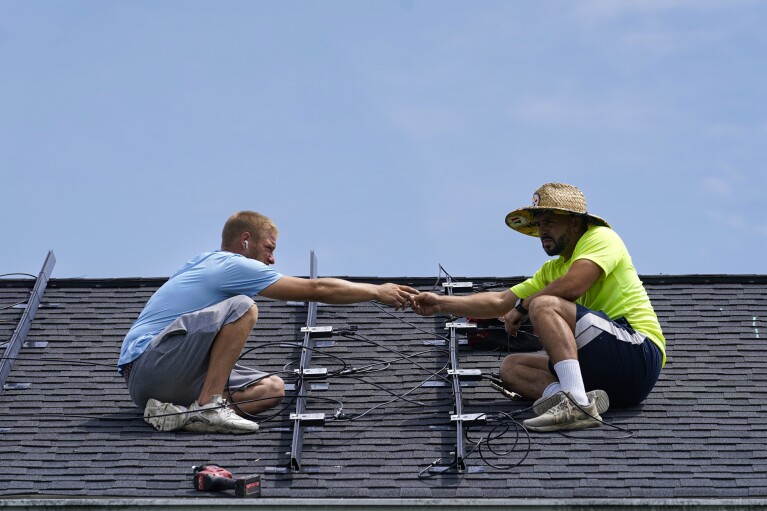 Brian Hubner, left, and Evin Berrios, install a solar panel on a rooftop in Frankfort, Kentucky, Monday, July 17, 2023 (AP Photo/Michael Conroy)