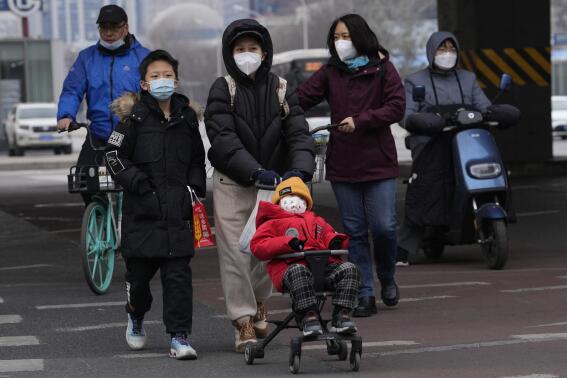 A child wearing a mask is pushed across a road in Beijing, Friday, Dec. 2, 2022. More cities eased restrictions, allowing shopping malls, supermarkets and other businesses to reopen following protests last weekend in Shanghai and other areas in which some crowds called for President Xi Jinping to resign. (AP Photo/Ng Han Guan)