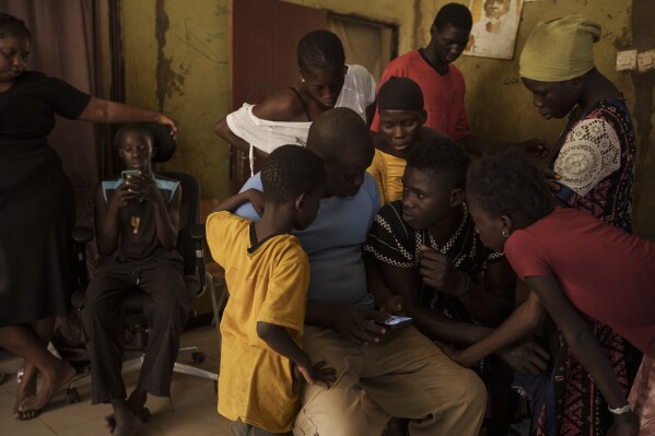 Papa Dieye, de 19 años, centro derecha, habla con su padre, Badara Dieye, mientras miran fotografías de su rescate en un teléfono celular, rodeado de otros familiares en Diogo, Senegal, el lunes 28 de agosto de 2023. (AP Foto/Felipe Dana)