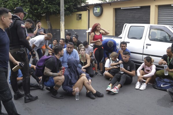 Staff members sit on a street after they were evacuated from the TC television channel station after a group of armed men broke onto their set during a live broadcast, in Guayaquil, Ecuador, Tuesday, Jan. 9, 2024. The country has seen a series of attacks after the government imposed a state of emergency in the wake of the apparent escape of a powerful gang leader from prison. (AP Photo/Cesar Munoz)