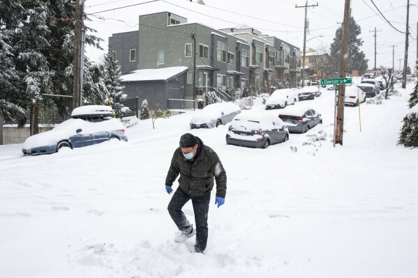 John Kramer walks down 42nd Avenue South in Columbia City as heavy snow blankets the Seattle area Saturday Feb. 13, 2021. A winter storm has blanketed the Pacific Northwest with ice and snow, leaving hundreds of thousands of people without power and disrupting travel. A winter storm has blanketed the Pacific Northwest with ice and snow, leaving hundreds of thousands of people without power and disrupting travel. (Bettina Hansen/The Seattle Times via AP)