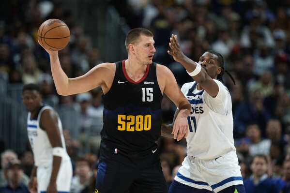 Denver Nuggets center Nikola Jokic, left, looks to pass the ball as Minnesota Timberwolves center Naz Reid defends during the second half of Game 2 of an NBA basketball second-round playoff series, Monday, May 6, 2024, in Denver. (AP Photo/David Zalubowski)