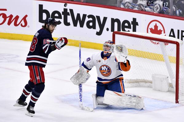 New York Islanders goaltender Semyon Varlamov (40) and Winnipeg Jets Kevin Stenlund (28) watch the puck as it rebounds after a shot during the first period of an NHL hockey game in Winnipeg, Manitoba, on Sunday, Feb, 26, 2023. (Fred Greenslade/The Canadian Press via AP)